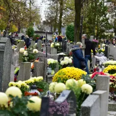 Ludzie odwiedzają cmentarz komunalny w Wieliczce, składając kwiaty i zapalając znicze.