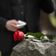 Czerwona róża na kamieniu, w tle osoba w czerni. Trudne chwile, gdy szukamy informacji, gdzie jest najbliższe krematorium.