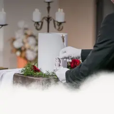 Uroczystość pogrzebowa w Toruniu. Biała urna, zdjęcie zmarłej, róże i świece.