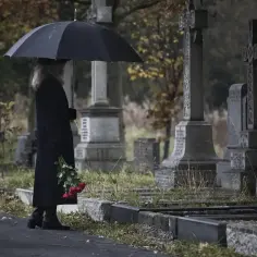 Smutna kobieta z parasolką i czerwonymi różami na cmentarzu. Pamiętaj, dlaczego nie wolno przynosić rzeczy z cmentarza do domu.