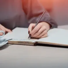 Dłoń pisze w notesie, szukając sposobu, jak sformułować intencję za zmarłego. Obok filiżanka kawy.