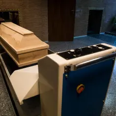 Drewniana trumna na taśmie transportowej przed krematorium.