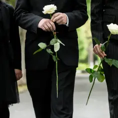 Trzy osoby w czarnych strojach niosą róże.
