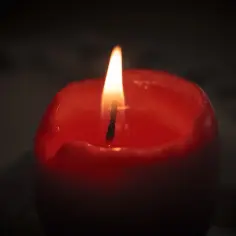 Płonąca, czerwona świeca. Wosk spływa po jej bokach, tworząc krople. W tle ciemność, jakby wspomnienia o tych, co brzesko ws odeszli.